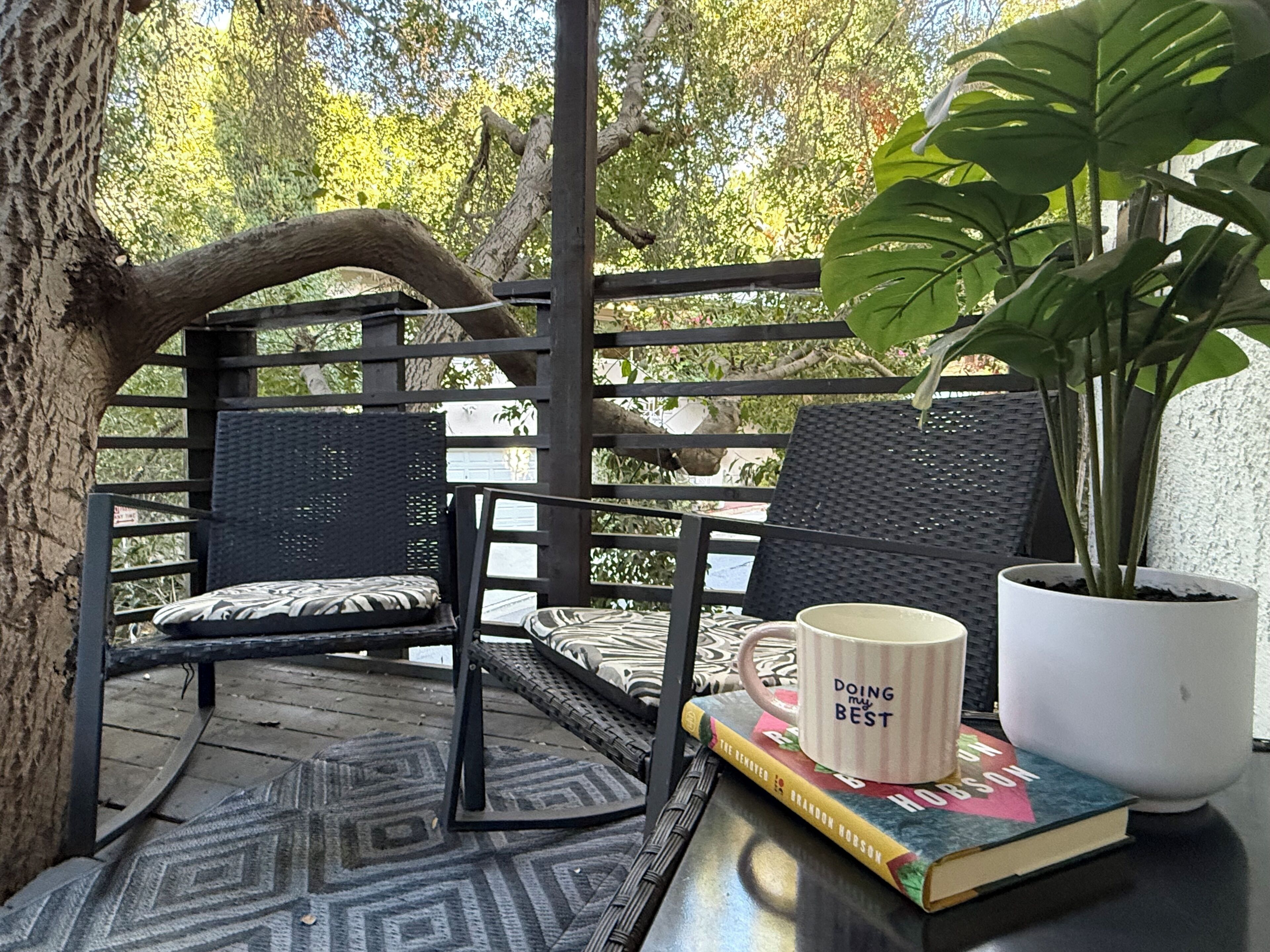 A wooden deck with a black metal chair and a table with a book and a mug.