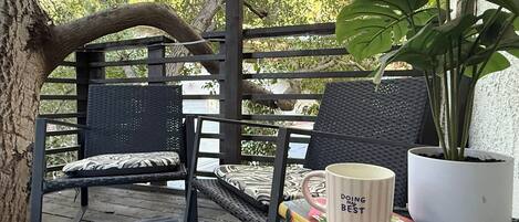 A wooden deck with a black metal chair and a table with a book and a mug.