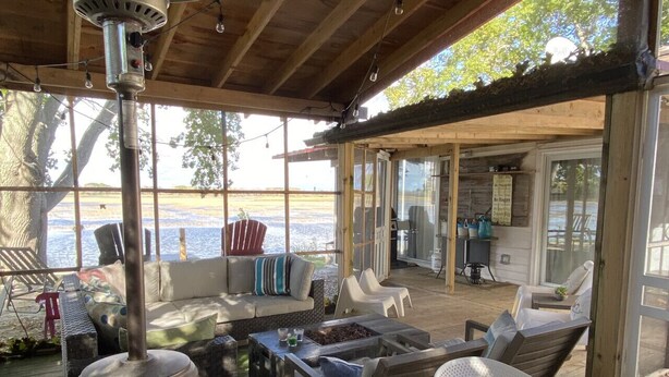 Eine Terrasse im Freien mit Holzboden, einem großen Metallheizstrahler, Gartenmöbeln und Blick auf das Wasser.