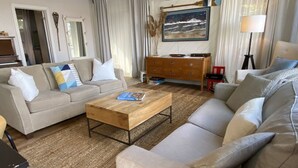 Ein Wohnzimmer mit beiger Couch, Couchtisch aus Holz, rotem Sessel und einer Lampe.