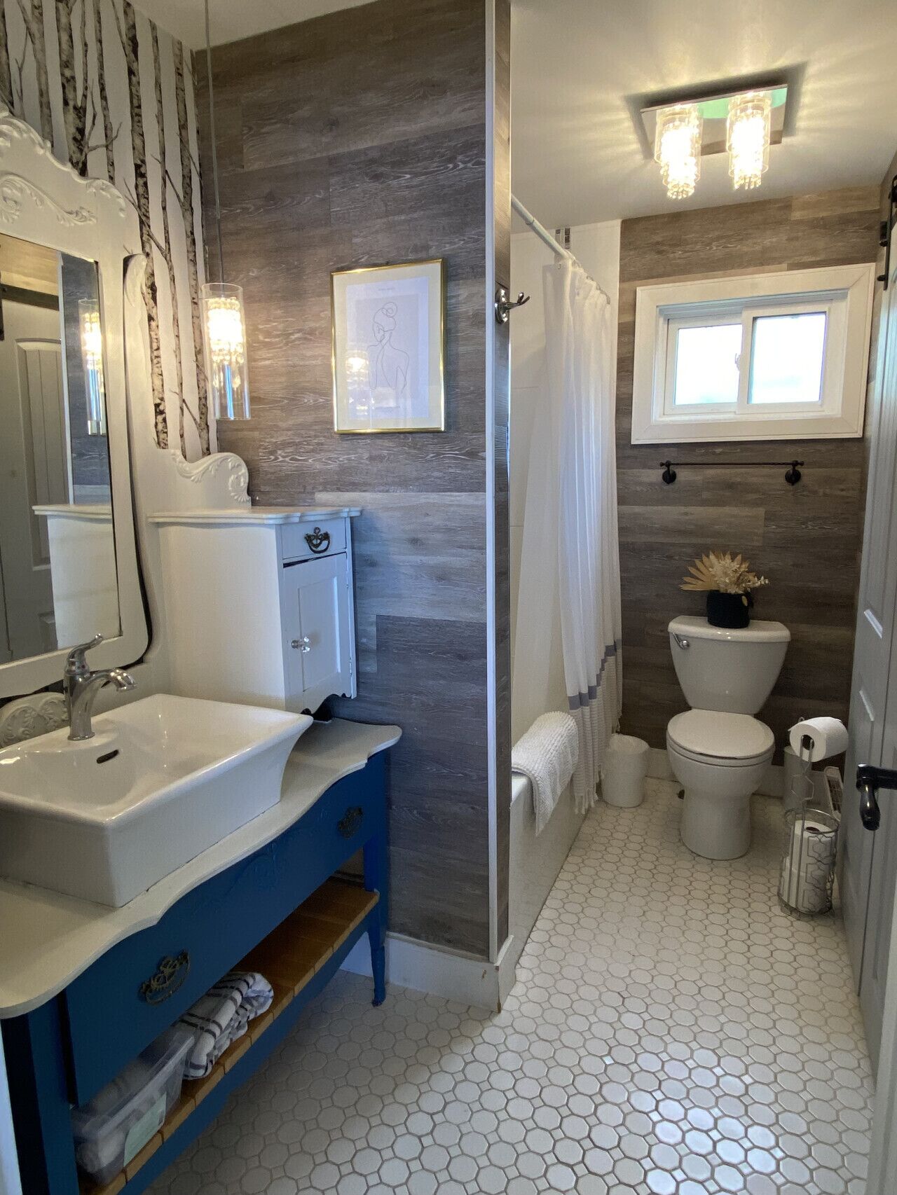 Ein Badezimmer mit weißem Waschbecken, blauer Waschtischunterschrank, einer Dusche mit Glastür, einer Toilette und einem Fenster über der Toilette.