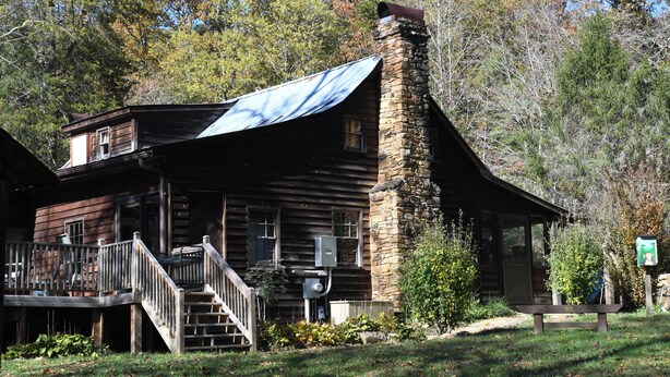 A rustic log cabin with a stone chimney, a covered porch, and a small deck. - Charming Shared Cabin at Project Chimps Sanctuary (Morganton)