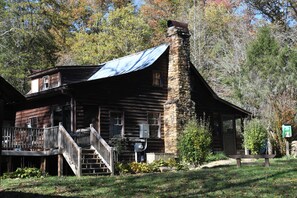 A rustic log cabin with a stone chimney, a covered porch, and a small deck.