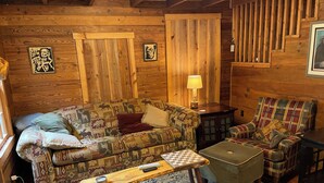 A cozy log cabin interior with a patterned sofa, plaid armchair, and a small wooden table. - Charming Shared Cabin at Project Chimps Sanctuary (Morganton)