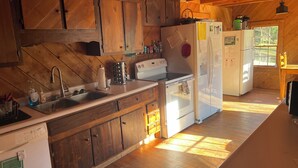 A kitchen with wooden cabinets, a sink, a stove, and a refrigerator. - Charming Shared Cabin at Project Chimps Sanctuary (Morganton)