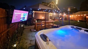 Patio con jacuzzi, una pantalla de televisión mostrando un menú y luces colgantes.
