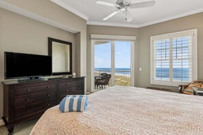 Une chambre à coucher comprenant un lit, une commode, un téléviseur, un ventilateur de plafond et un balcon avec vue sur l’océan.
