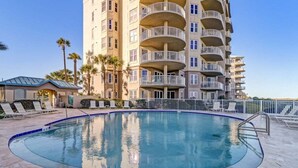A swimming pool with a surrounding deck, a tall building with balconies, and palm trees.