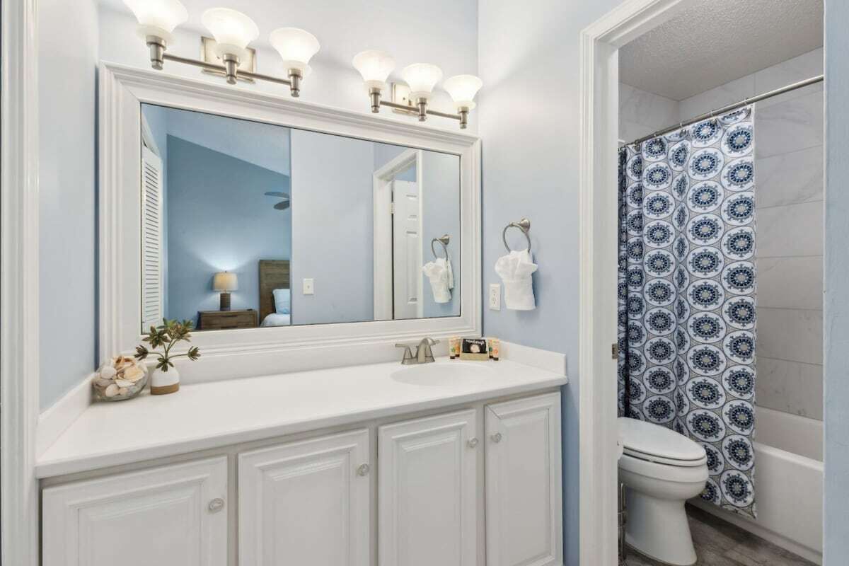 A bathroom with a large mirror, a sink, a toilet, and a shower curtain.