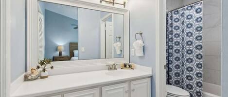 A bathroom with a large mirror, a sink, a toilet, and a shower curtain.