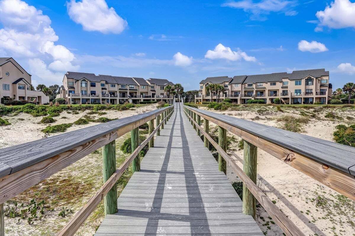 A wooden boardwalk leading to a beachfront hotel with multiple-story buildings.
