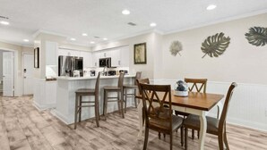 Une cuisine moderne avec des meubles blancs, un îlot central et un coin repas doté de chaises en bois.