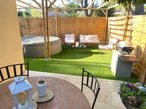 Eine Terrasse mit einem runden Tisch, Stühlen, einer Laterne, einem Grill und einem Whirlpool.