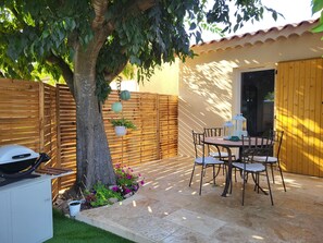Eine Terrasse mit Tisch, Stühlen, einem Grill und einem Baum.