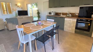 A modern kitchen with green cabinets, a dining area with a wooden table and chairs, and a TV in the living area. - L'An'Phi- Charming house with outdoor spa (Vaison-la-Romaine)