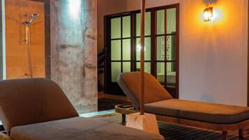 A room with two lounge chairs, a wooden floor, a large window with a view, and a wall-mounted light fixture.