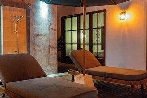 Quarto com duas poltronas, piso de madeira, uma janela ampla com vista e luminária fixada na parede.