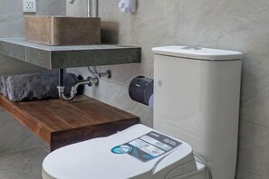 Une salle de bain au design moderne, dotée d’un lavabo en marbre, d’un banc en bois et de toilettes équipées d’un panneau de commande.