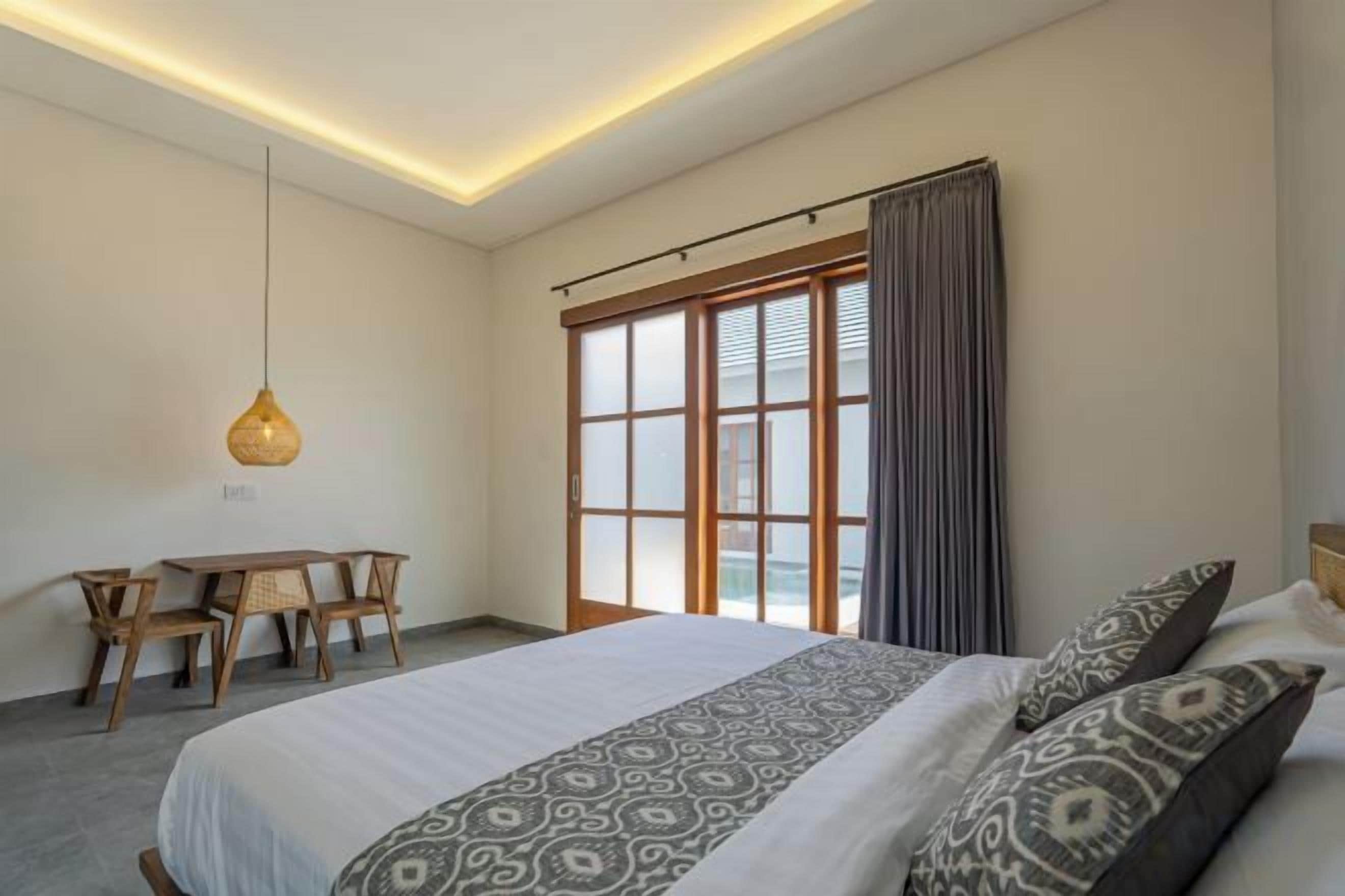A bedroom with a large bed, a desk, and a hanging light fixture.