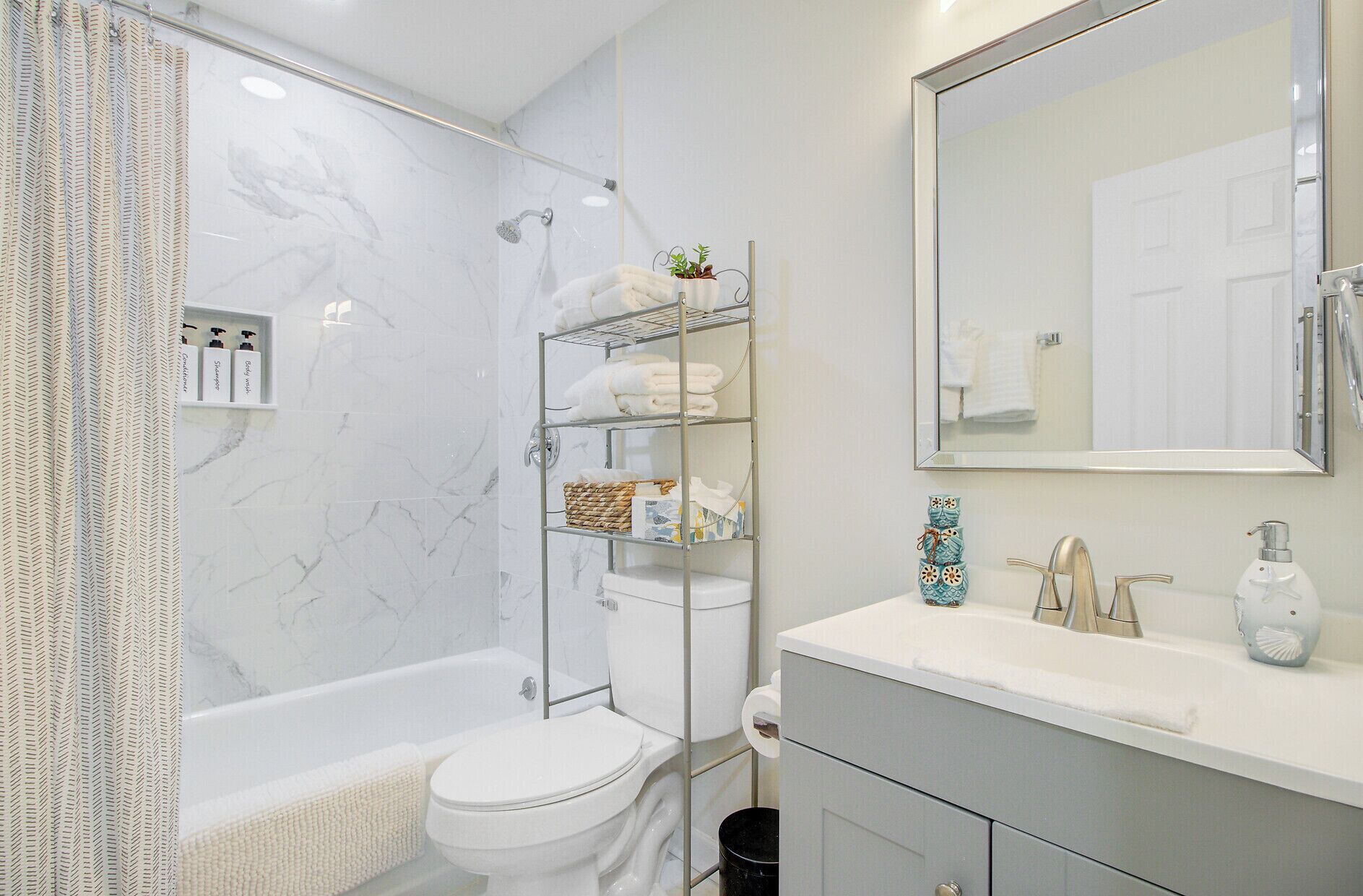 Un baño moderno con bañera, inodoro y ducha. Hay un estante con artículos de aseo y un espejo sobre el lavabo.