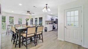 Une cuisine moderne avec des meubles blancs, un four à micro-ondes et une cuisinière. On y trouve un coin repas avec une table et des chaises, ainsi qu’un ventilateur de plafond.