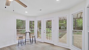 Une pièce spacieuse avec de grandes fenêtres, un ventilateur de plafond et une petite table avec des tabourets.