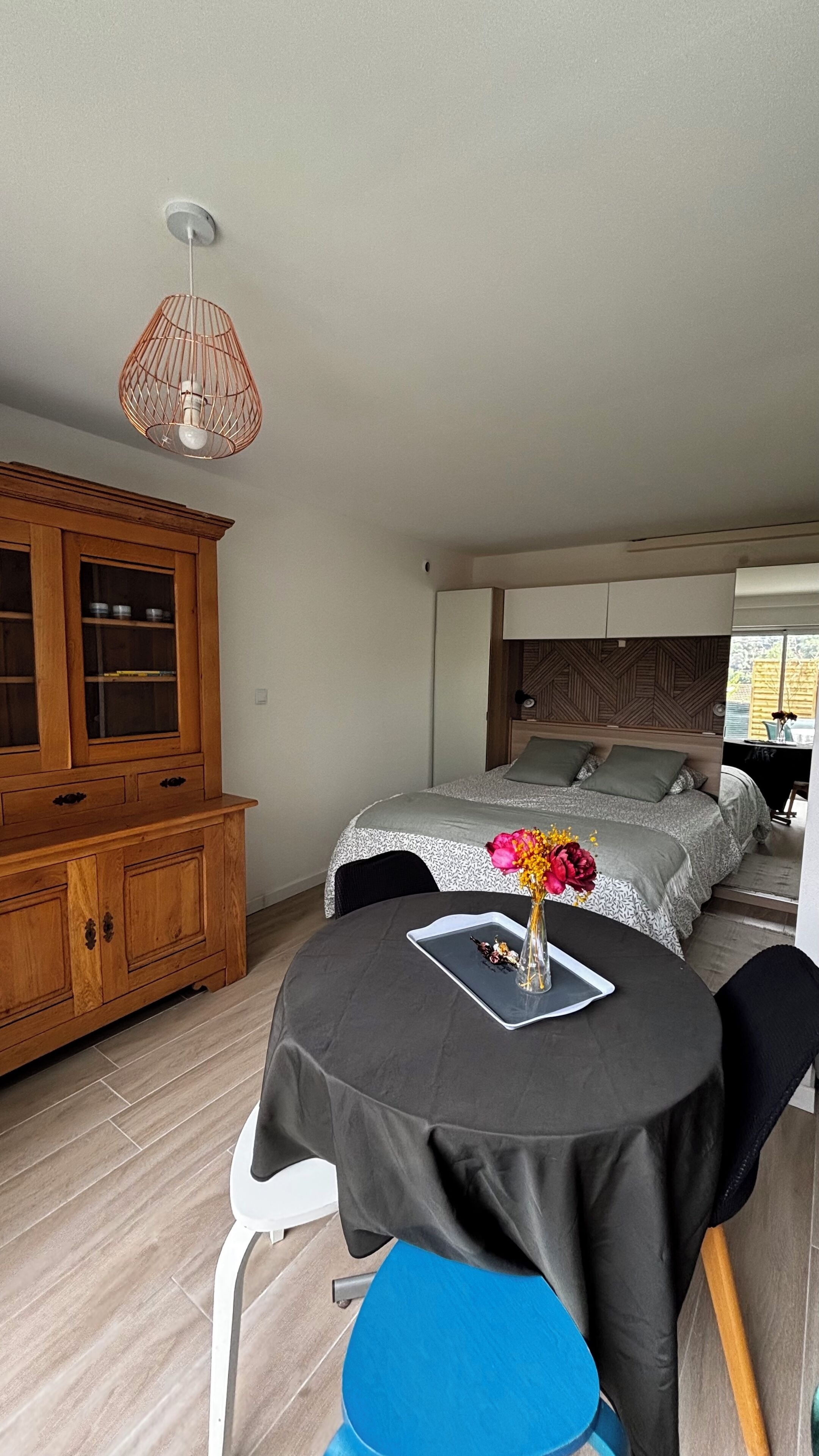 Ein Schlafzimmer mit einem Bett, einem Holzschrank, einem Tisch mit einer Vase und einer Hängeleuchte.