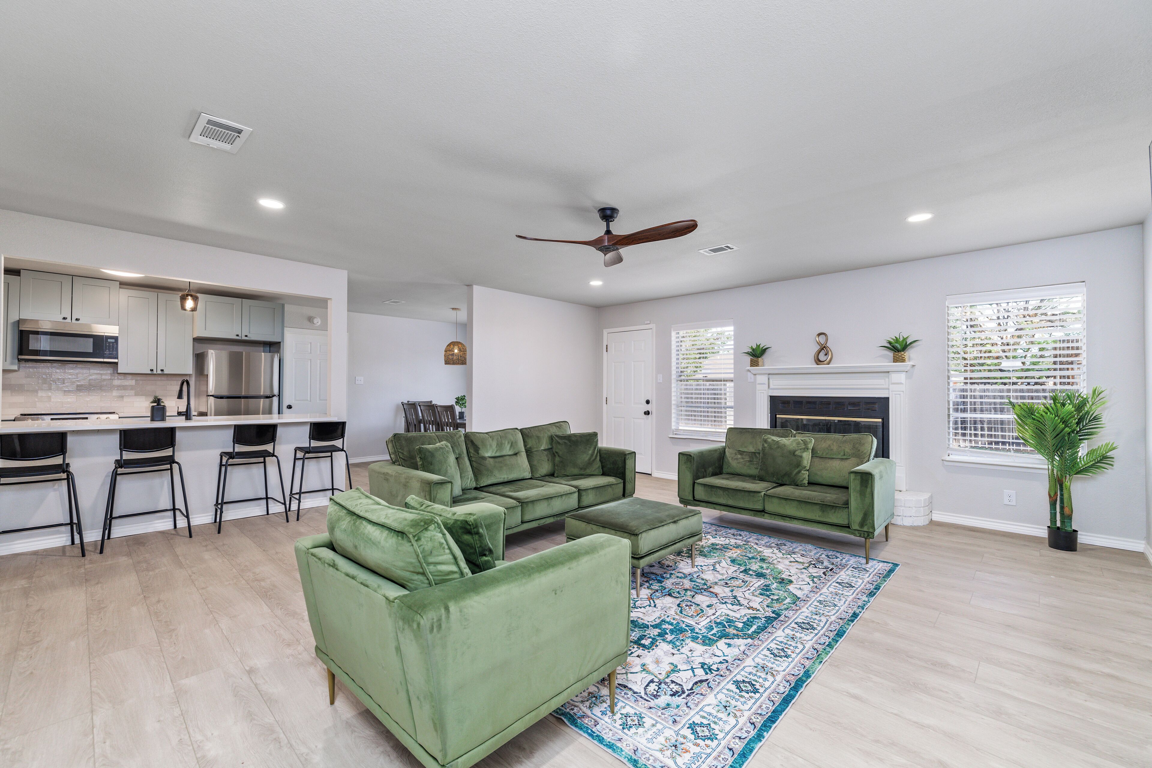 A modern living room with a green sofa set, a dining area with bar stools, and a kitchen with stainless steel appliances.
