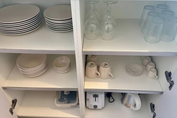 A kitchen with white cabinets, a coffee maker, and various kitchenware including plates, cups, and wine glasses.