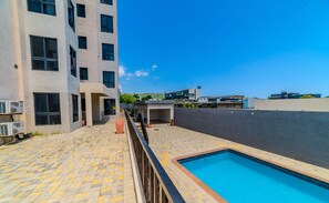 A rooftop swimming pool with a tiled deck, surrounded by a building with multiple windows and a flat roof. - Platinum 22 & you, Luxury Apartment (Kingston)