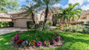 A residential property with a well-maintained garden, a driveway, and a two-story house with a tiled roof. - Lakefront Retreat in Prestigious Master Reserve at Lely Resort (Naples)