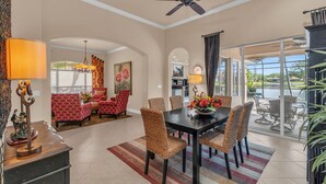 A spacious dining area with a black table and wicker chairs, a red patterned sofa, and a ceiling fan. - Lakefront Retreat in Prestigious Master Reserve at Lely Resort (Naples)