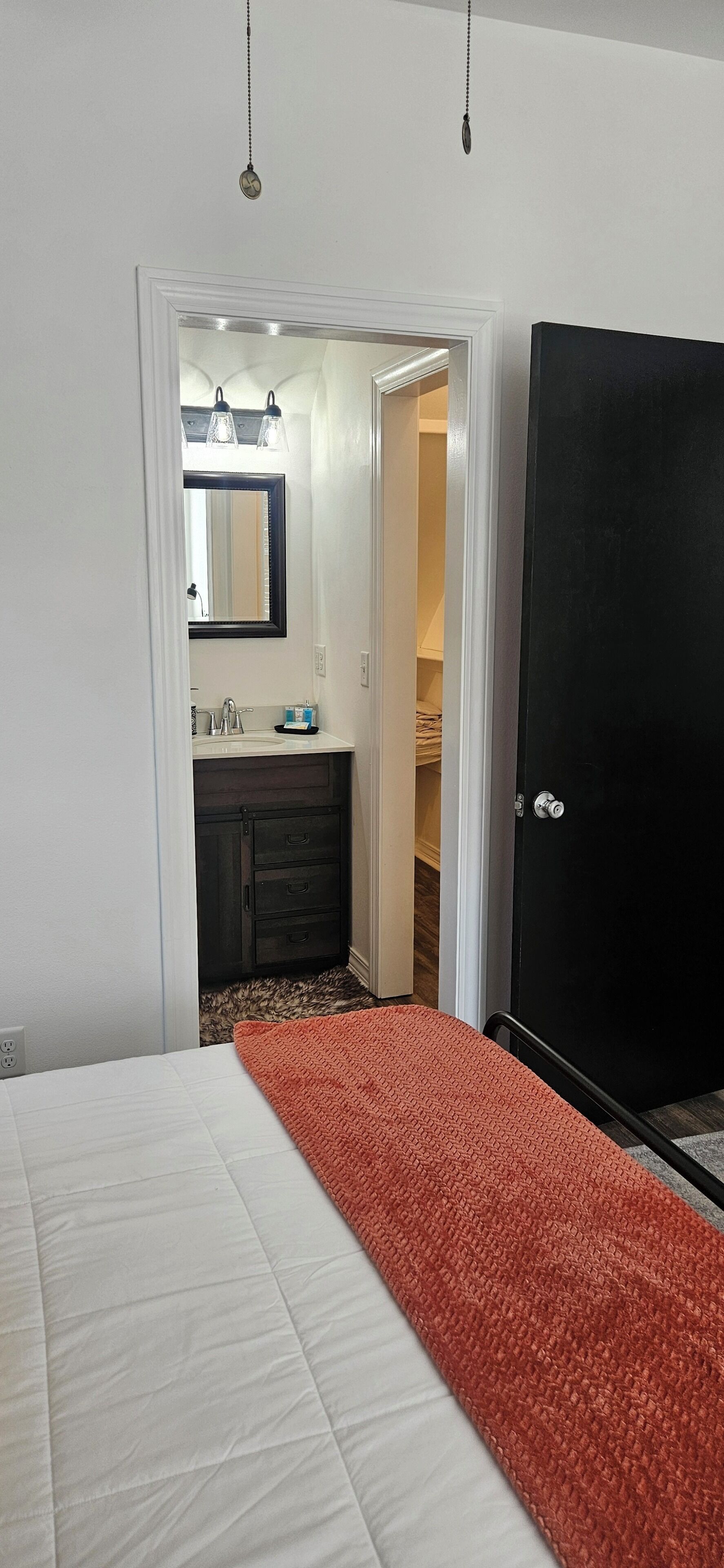 A bedroom with a bed, a wardrobe, a bathroom with a mirror, and a door leading to another room.