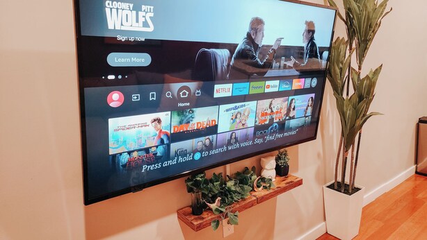 A flat-screen TV mounted on a wall displaying a streaming service interface with various movie options. - Prime / 2 King Beds / 65" TV / Jefferson Hospital (Philadelphia)