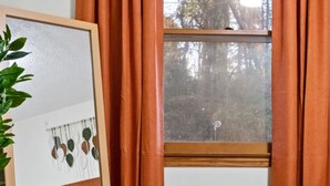 Ein Schlafzimmer mit einem Bett, einem großen Spiegel, einem Fenster mit Vorhängen und einer Pflanze.
