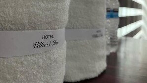 Three white towels with "HOTEL Villa's Inn" printed on them, placed on a wooden surface. - Hotel VillaS INN (León)