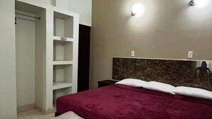 A bedroom with a bed, a bench, a wardrobe, and a headboard with wall lights. - Hotel VillaS INN (León)