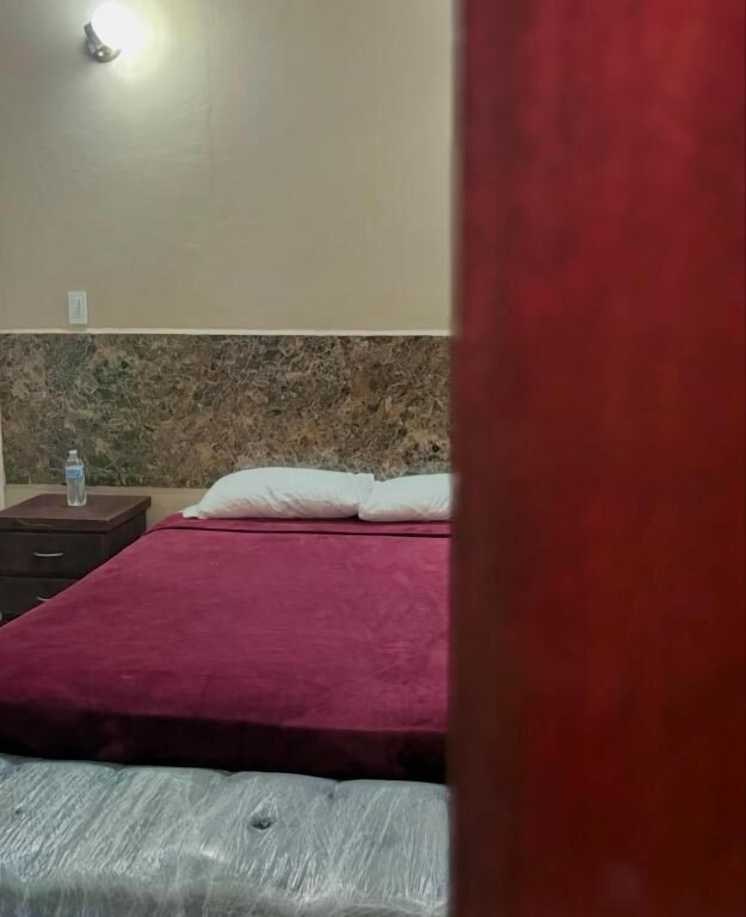 A room with a bed, a nightstand, a water bottle, and a wall-mounted light.