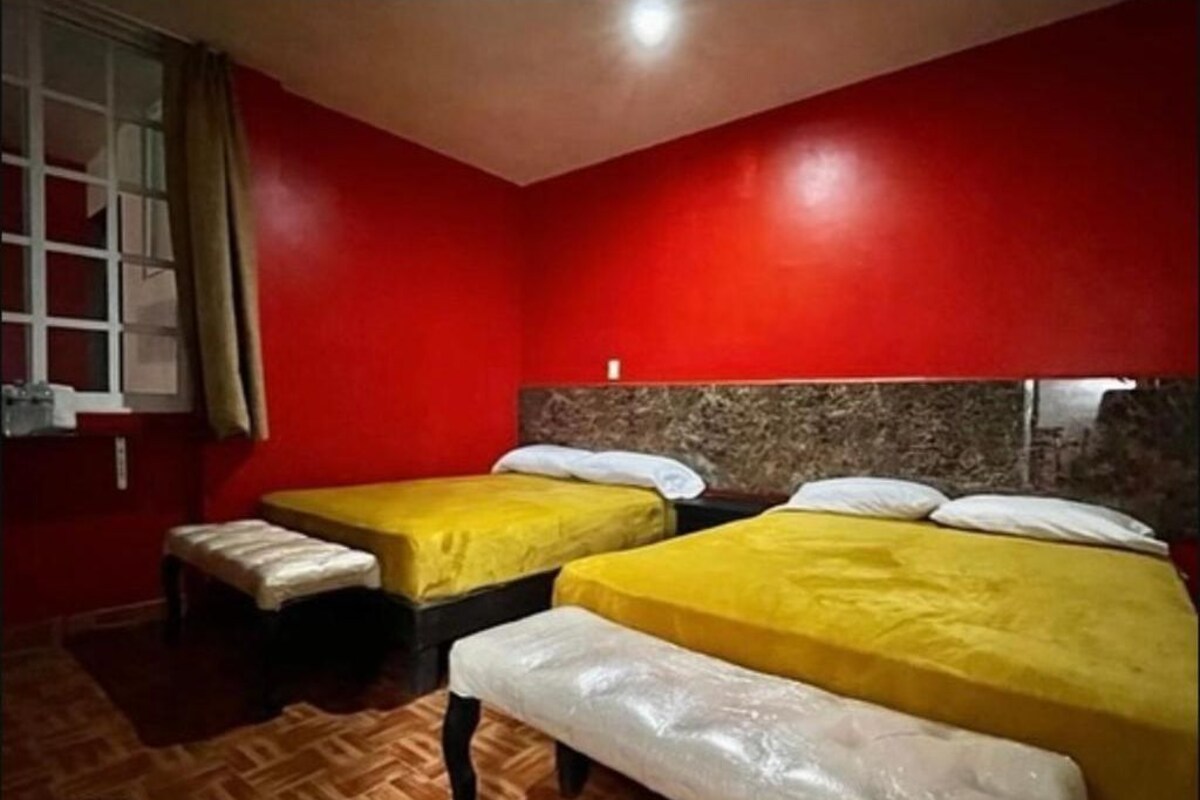 A hotel room with two beds, a wooden floor, and red walls.