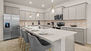 Una cocina moderna con una isla central, electrodomésticos de acero inoxidable e iluminación colgante.