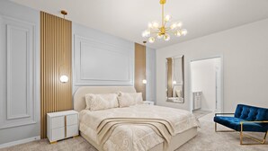 Un dormitorio con una cama grande, mesitas de noche, un espejo, una silla azul y un candelabro.