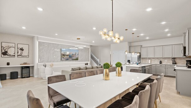 Un comedor amplio con una gran mesa blanca, varias sillas y una lámpara moderna.