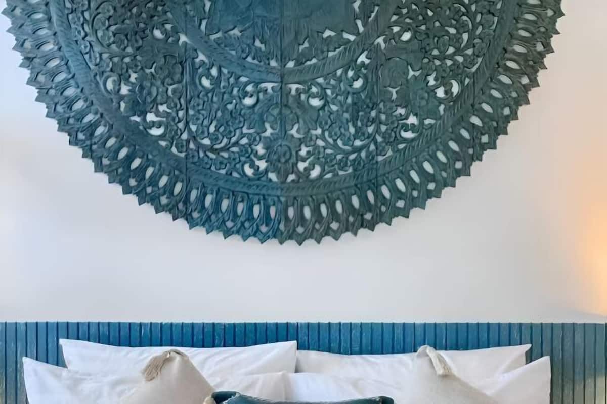 A room with a blue headboard, white pillows, and a decorative wall hanging.
