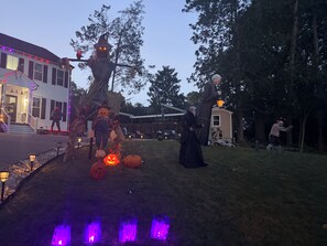 A residential area with a house decorated for Halloween, including a scarecrow and pumpkins.
