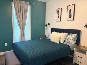 A bedroom with a bed, a bedside table, a lamp, and a window with curtains.