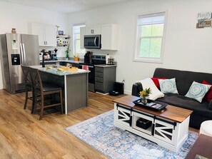 Een moderne keuken met een centraal eiland, een eethoek met een houten tafel, en een zithoek met een bank en decoratieve kussens.