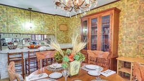 A dining area with a wooden table set for six, surrounded by chairs. There is a kitchen in the background with a white countertop and various appliances. - Rural Retreat: ‘Cypress Lake’ By Roosevelt St Park (Morton)