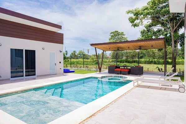 Et moderne hus med swimmingpool, udendørs møbler og en overdækket terrasse.