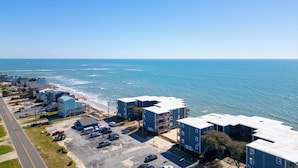 A coastal residential area with multiple two-story buildings, a parking lot, and a view of the ocean. - Steps to Sand! 3rd-Floor North Topsail Beach Condo (North Topsail Beach)