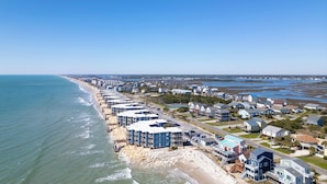A coastal residential area with beachfront properties, including multi-story buildings and single-family homes, along a sandy beach. - Steps to Sand! 3rd-Floor North Topsail Beach Condo (North Topsail Beach)